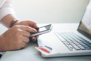 Persona utilizando un móvil junto a un portátil y una tarjeta bancaria, imagen relacionada con la suspensión de pagos.